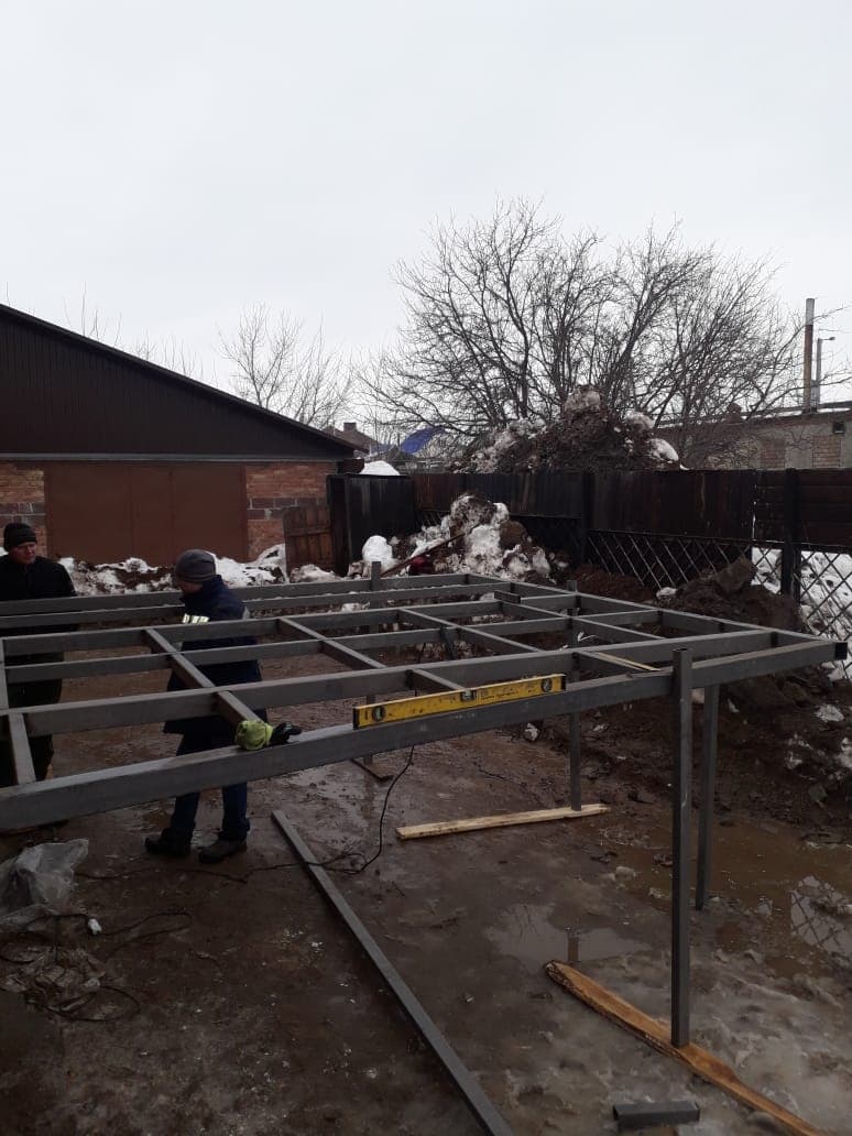 Двое мастеров выставляют сварной каркас на опорах по уровню